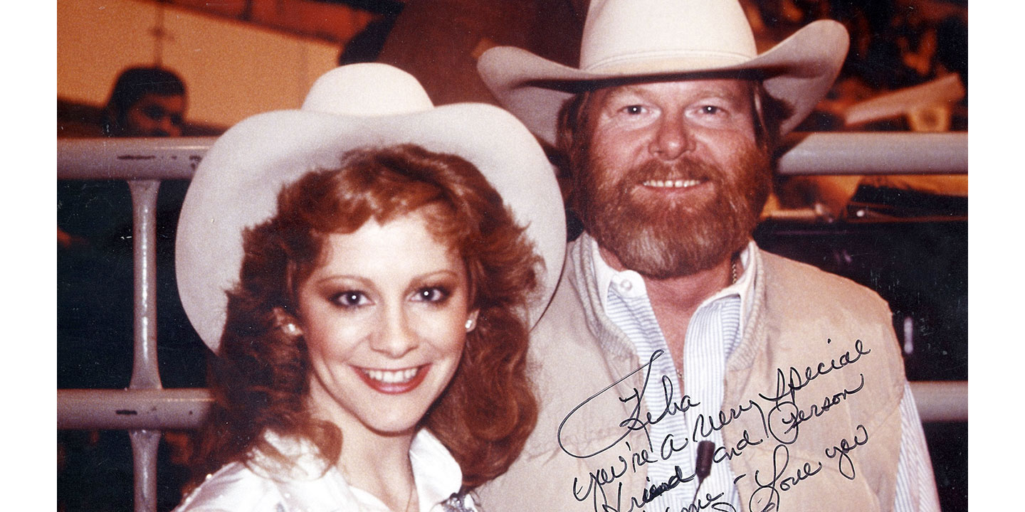 Reba McEntire and Red Steagall, both with red hair and wearing white cowboy hats, pose for a photo. The photo is autographed with a marker.